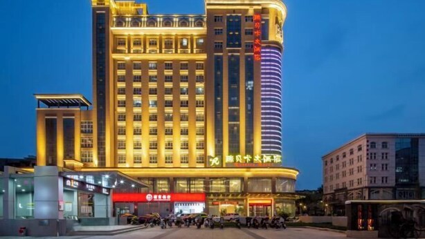 A multi-story hotel with a prominent entrance, a large parking area, and several ground-level shops. - Rebecca Hotel (Zhengzhou)