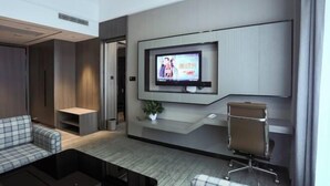 A modern hotel room with a flat-screen TV mounted on the wall, a sofa, a small table, and a chair. - Rebecca Hotel (Zhengzhou)