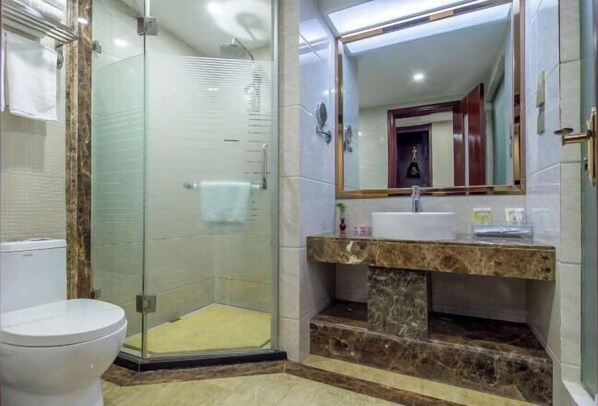 Ein Badezimmer mit einer Duschkabine, einer weißen Toilette, einem мраморным Waschbecken und einem Spiegel darüber.