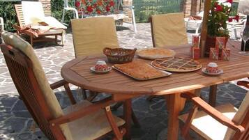 An outdoor dining area with a round wooden table, cushioned chairs, and a view of the countryside.