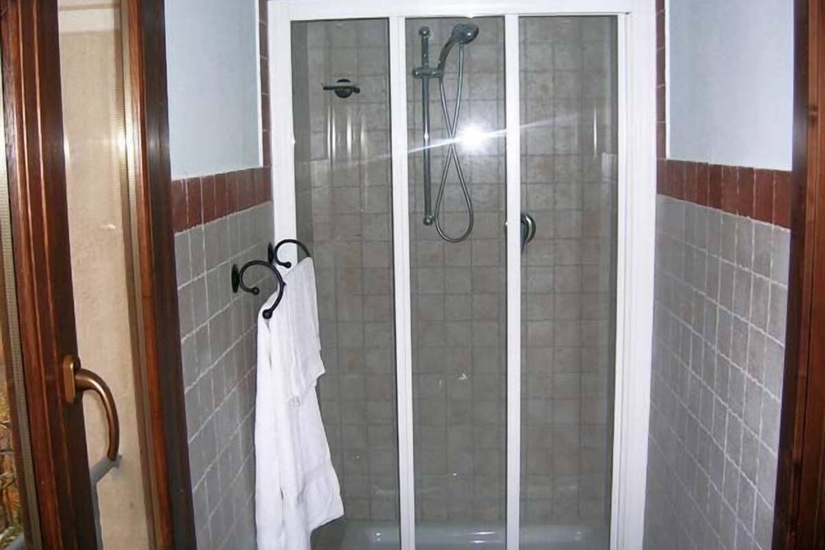 Un espace de douche entièrement vitré, avec une serviette blanche suspendue à un crochet.