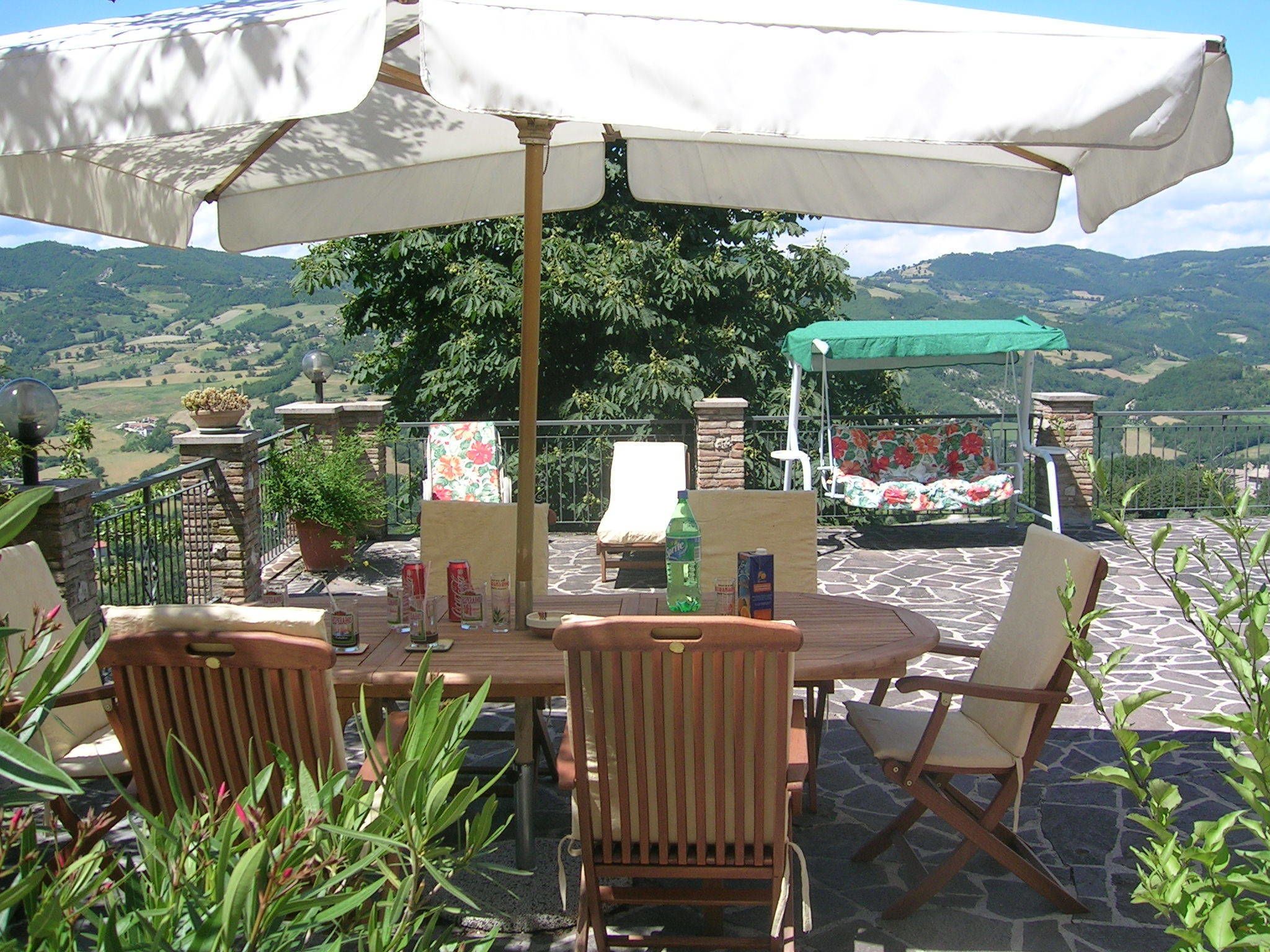 An outdoor patio with a table and chairs, surrounded by potted plants and a view of the countryside.