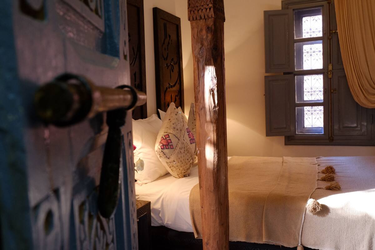 Ein Schlafzimmer mit Holztür, einem Bett mit weißer Bettwäsche und einem Fenster mit Vorhängen.