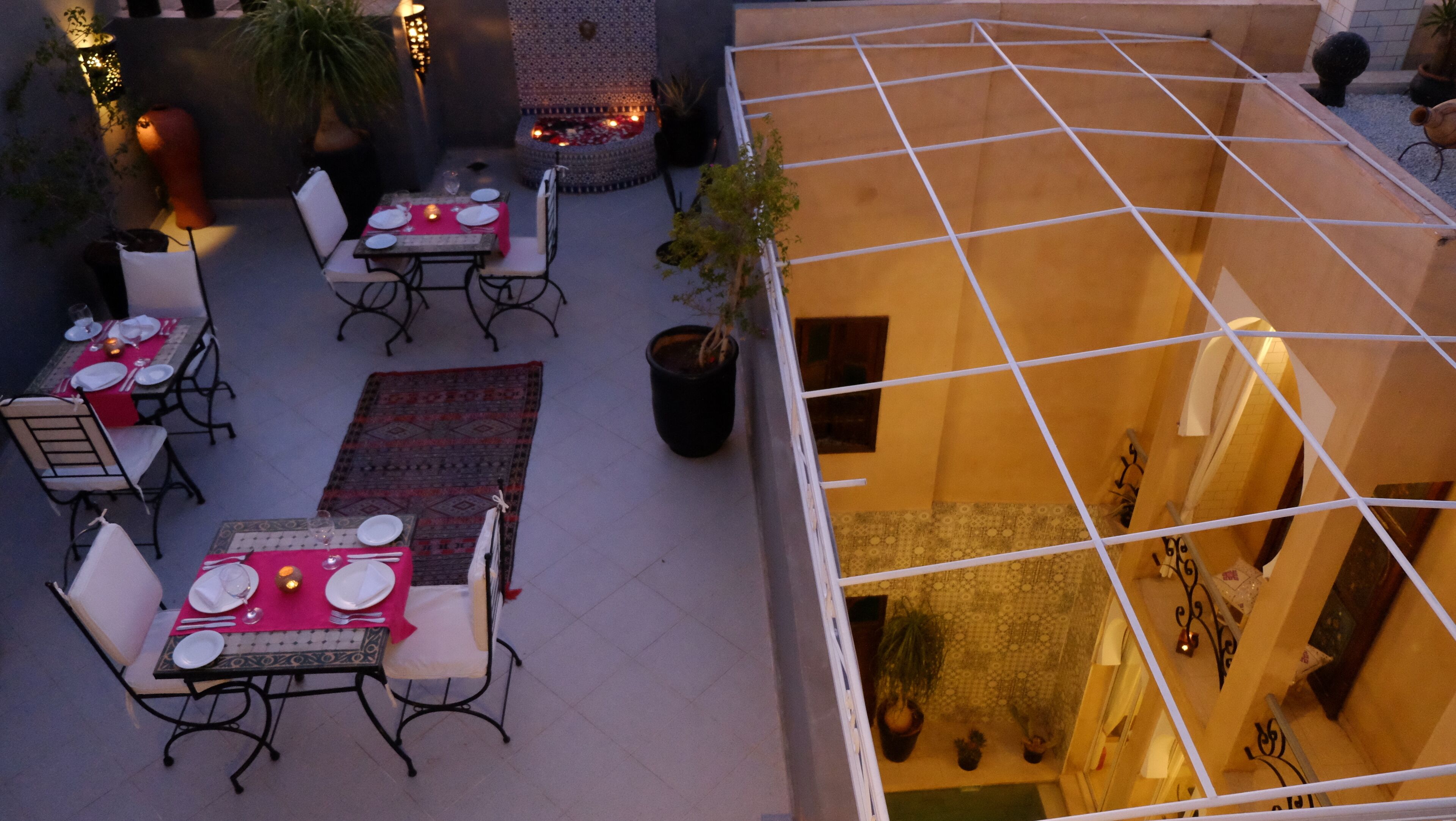 An outdoor dining area with tables and chairs, a patterned rug, and potted plants.
