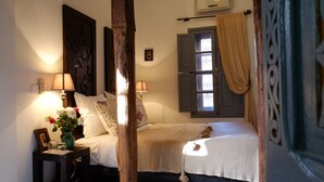 Un dormitorio con cama, dos lámparas de noche, una mesita de noche, un cuadro enmarco, un florero con flores y una ventana con cortinas.