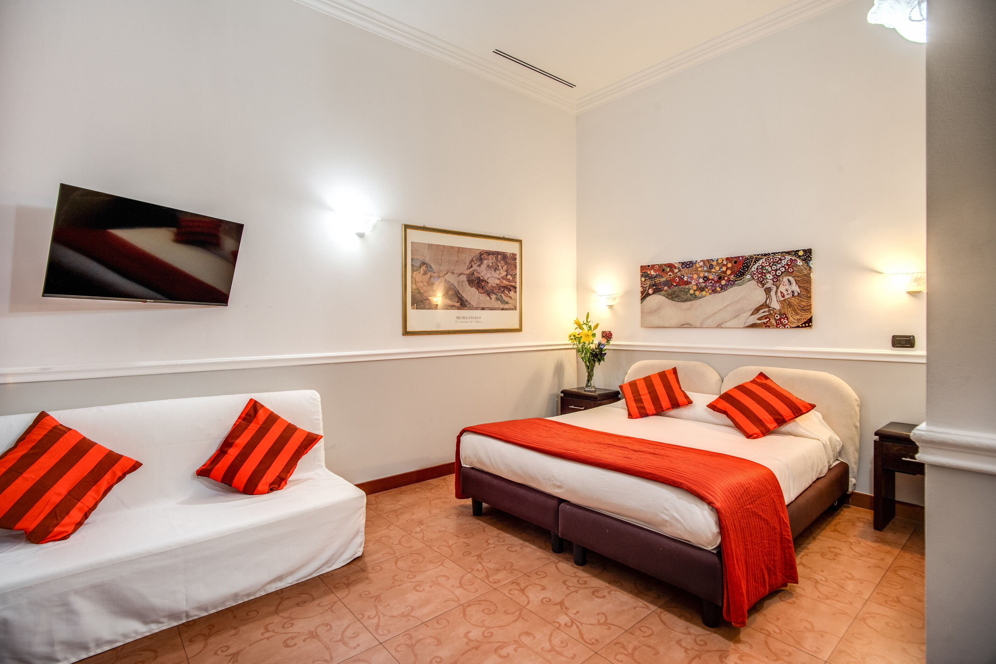 Habitación de hotel con cama, sofá y dos cuadros en la pared.