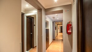 Ein Hotelkorridor mit an der Wand montiertem Feuerlöscher, einer Tür mit einem Schild darüber und einem Gang, der zu einem anderen Zimmer führt.
