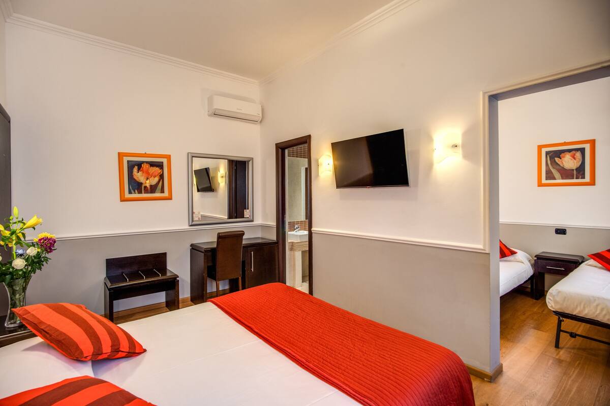 A hotel room with a bed, a desk, a chair, a TV, and a bathroom visible through an open door.