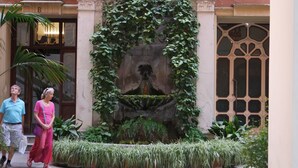 Ein Innenhof mit einem Brunnen, umgeben von Grünflächen und architektonischen Details.