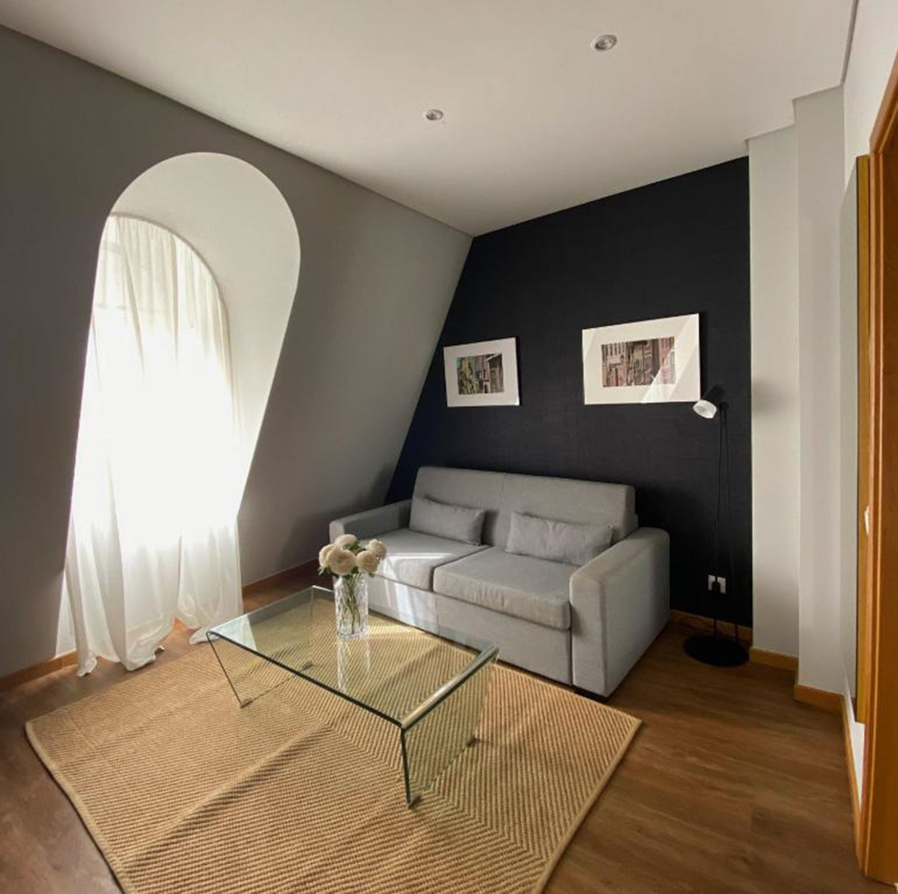 Una sala de estar moderna con un sofá gris, una mesa de centro de cristal y dos cuadros en la pared.