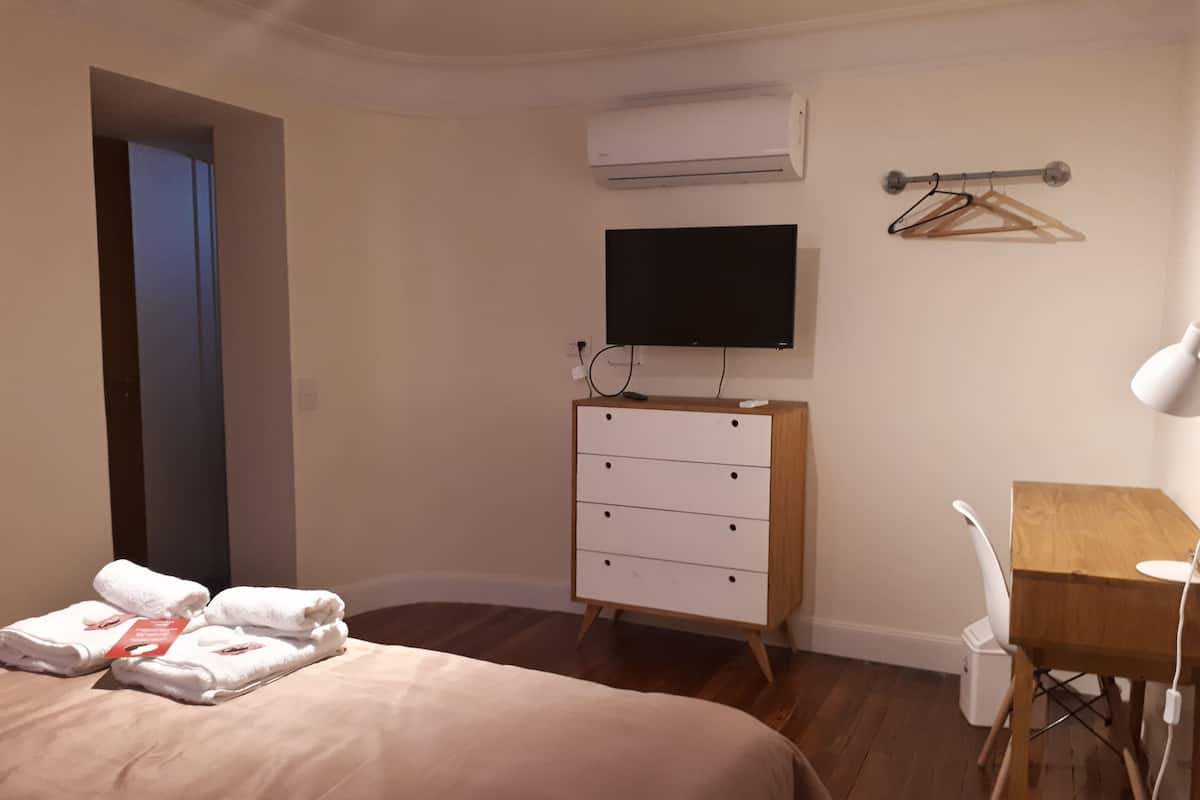 Ein Hotelzimmer mit Bett, Schreibtisch, Stuhl, Kommode, Klimaanlage und Fernseher.