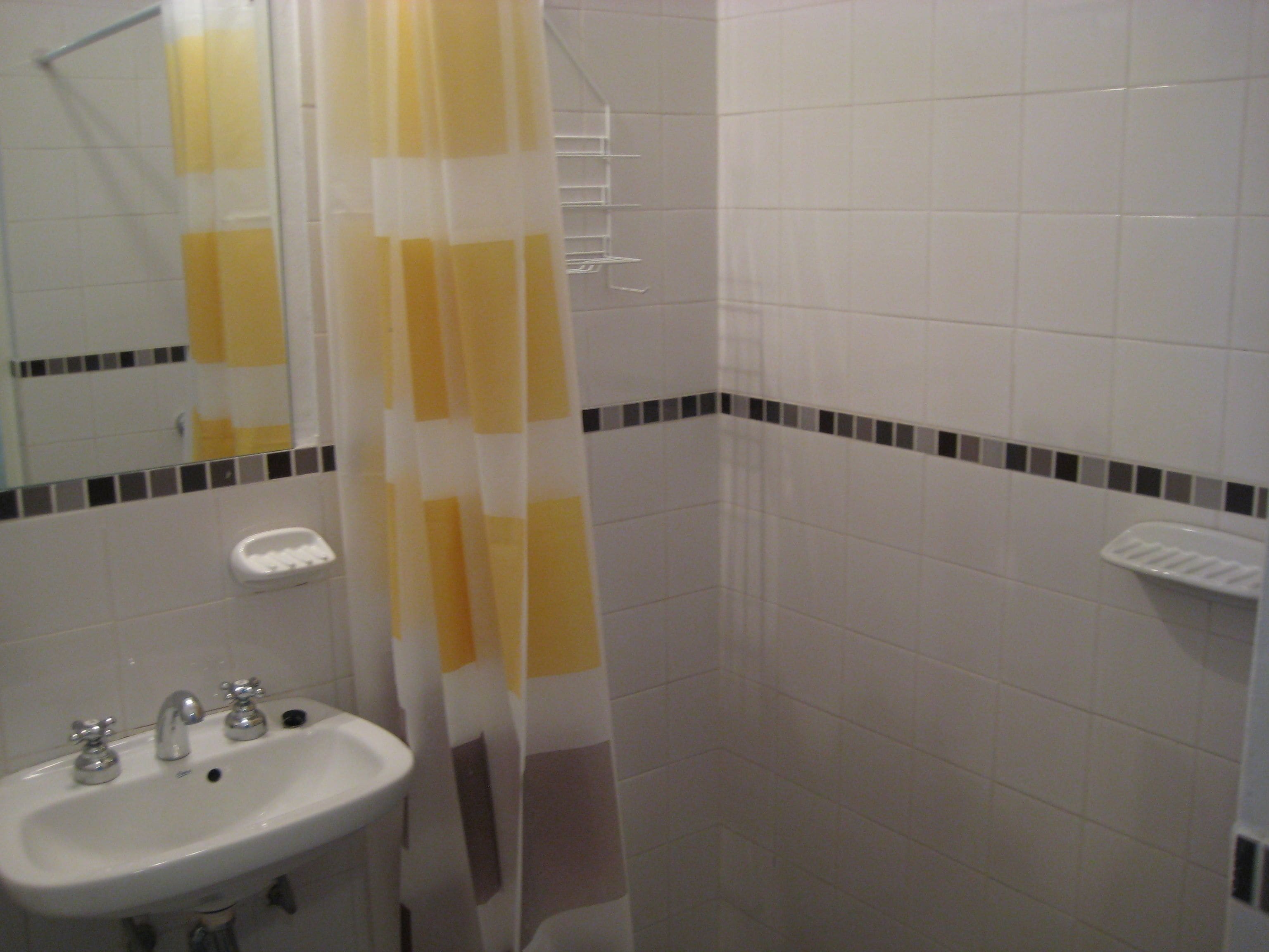 Une salle de bain avec un lavabo blanc, un miroir et un rideau de douche.