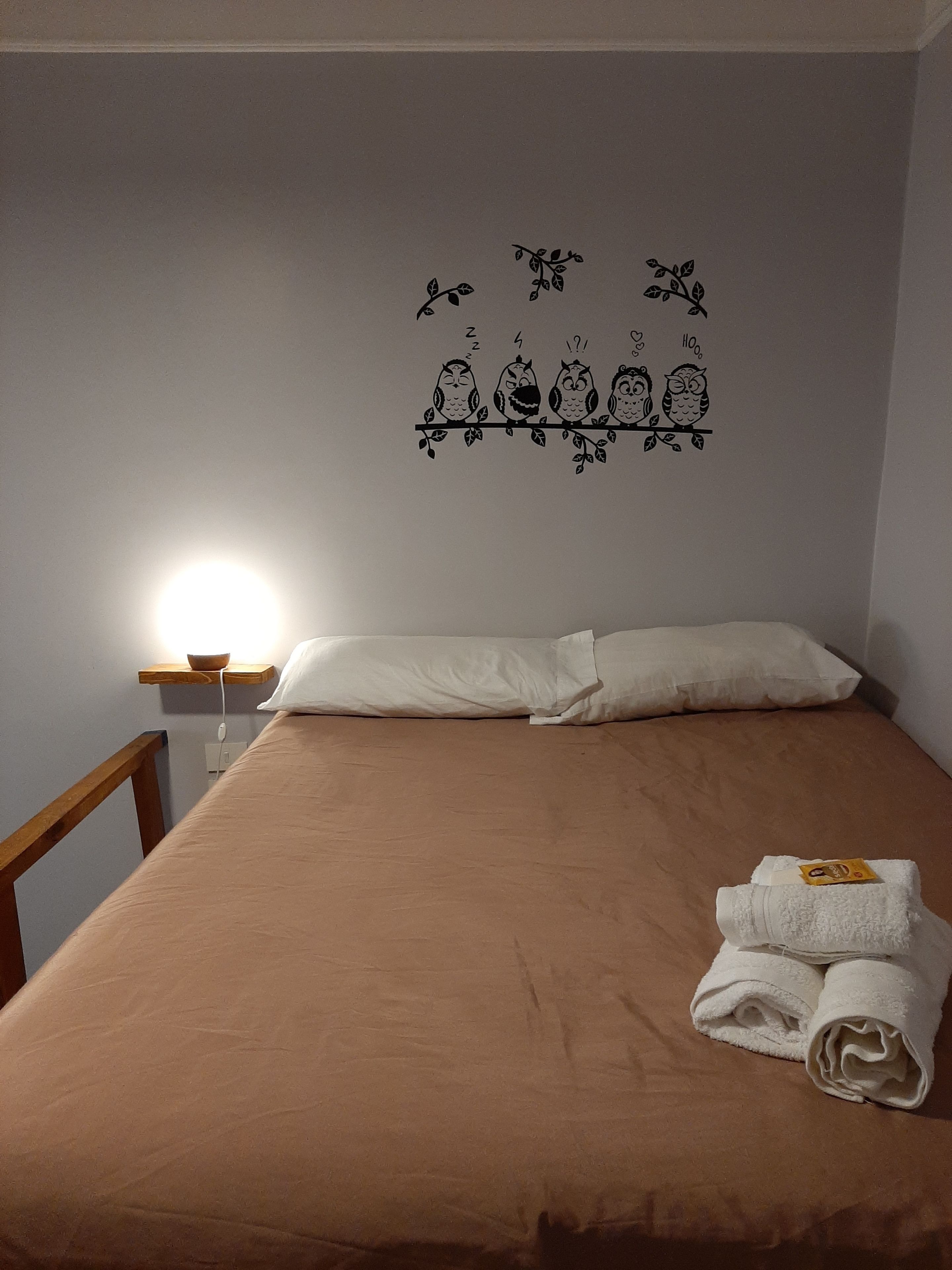 A neatly made bed with a brown bedspread, white pillows, and a set of folded towels on the right side.