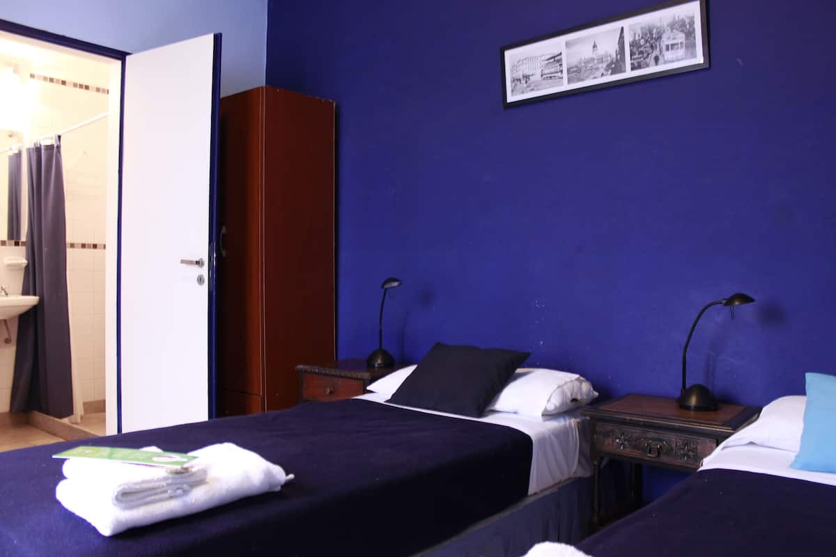 Ein Hotelzimmer mit zwei Betten, einem Schrank, einem Nachttisch mit Lampe und einem gerahmten Bild an der Wand.