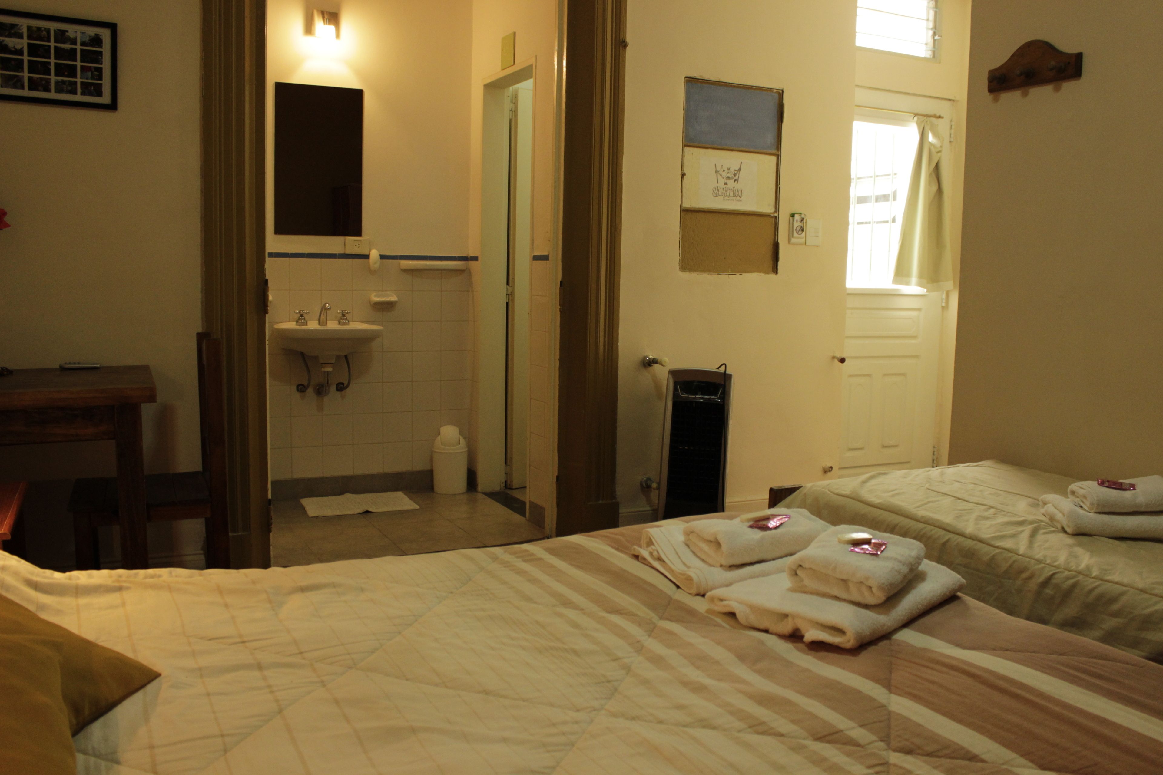 A hotel room with two beds, a bathroom with a sink, and a window with curtains.