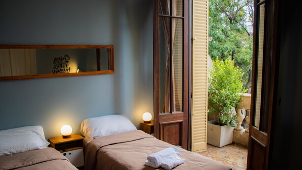 Een hotelkamer met twee bedden, een nachtkastje met een lamp, een spiegel en uitzicht op groen.