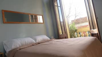 A bedroom with a large bed, a window with a view of the outside, and a mirror on the wall.