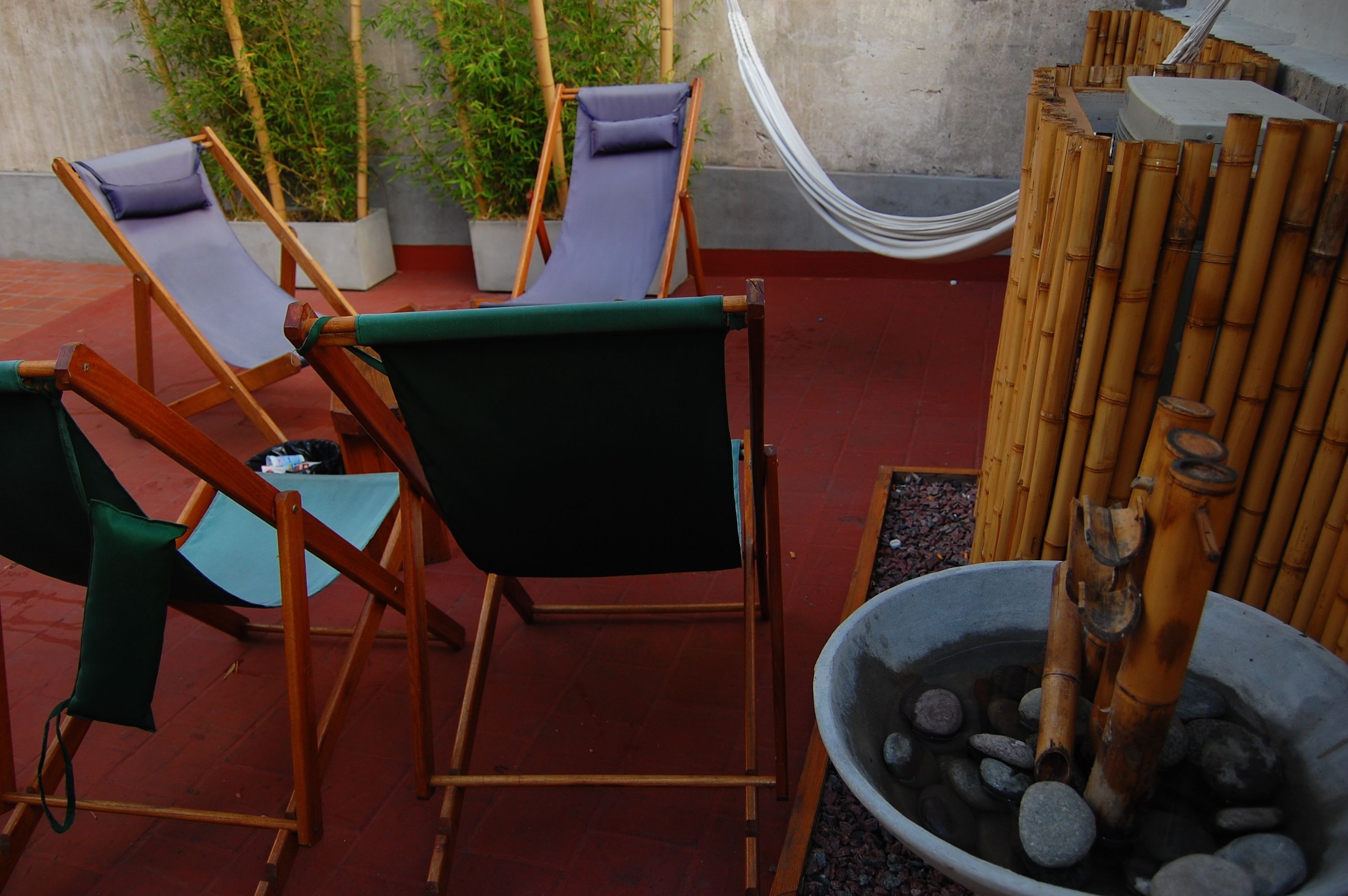 A patio area with two wooden lounge chairs, a hammock, and a bamboo water feature.