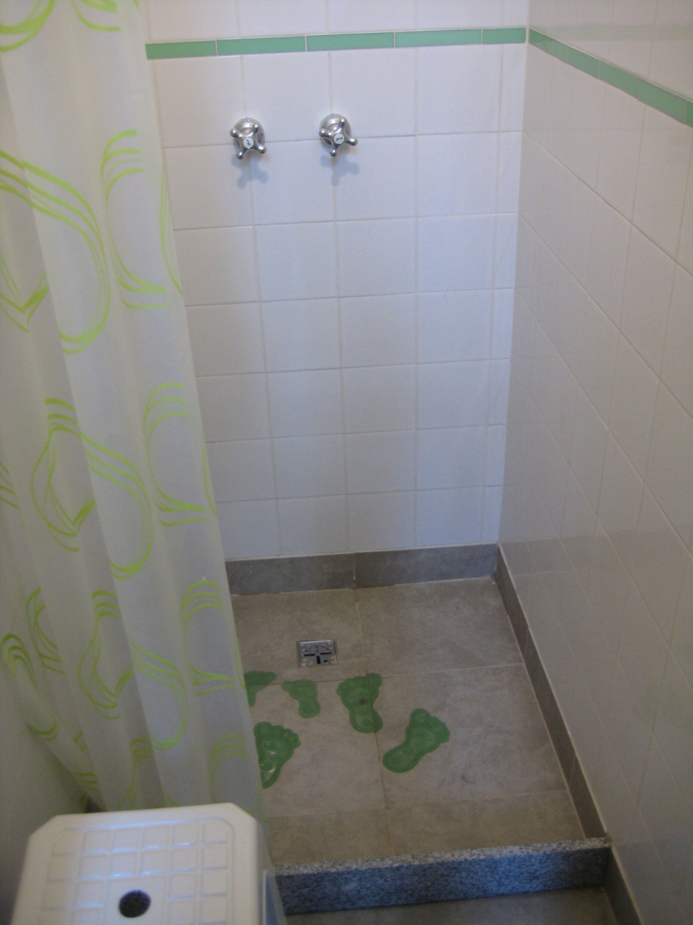 Un baño pequeño con azulejos blancos, una cortina de ducha con motivos de hojas verdes y un inodoro.