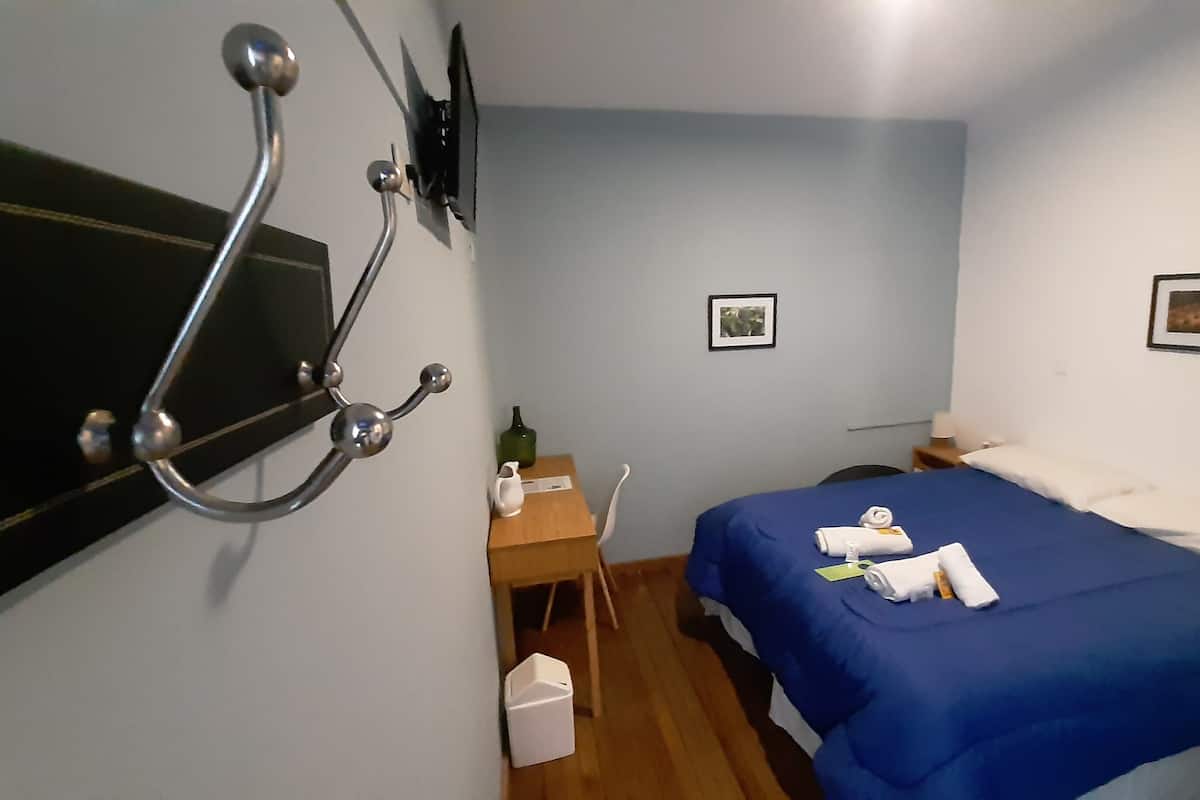 Ein Hotelzimmer mit Bett, Schreibtisch, Stuhl, einem an der Wand montierten Fernseher und zwei gerahmten Bildern.
