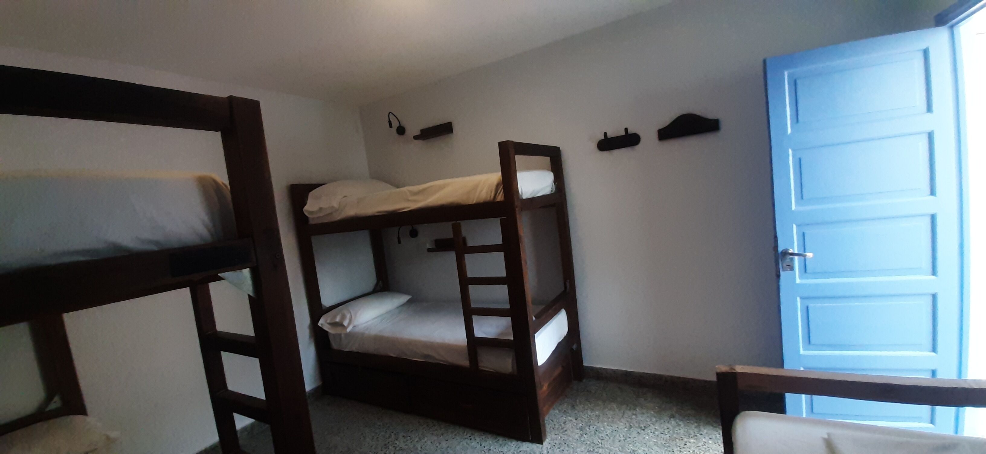Una habitación con dos literas, un estante pequeño con auriculares y una puerta azul.