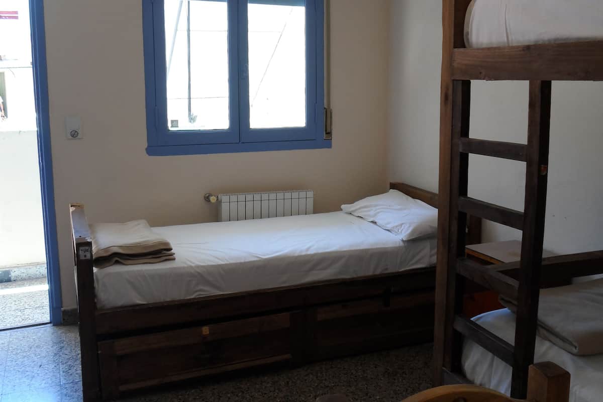 Ein kleines Zimmer mit einem Einzelbett, einem Fenster, einer Heizung und einem Etagenbett.