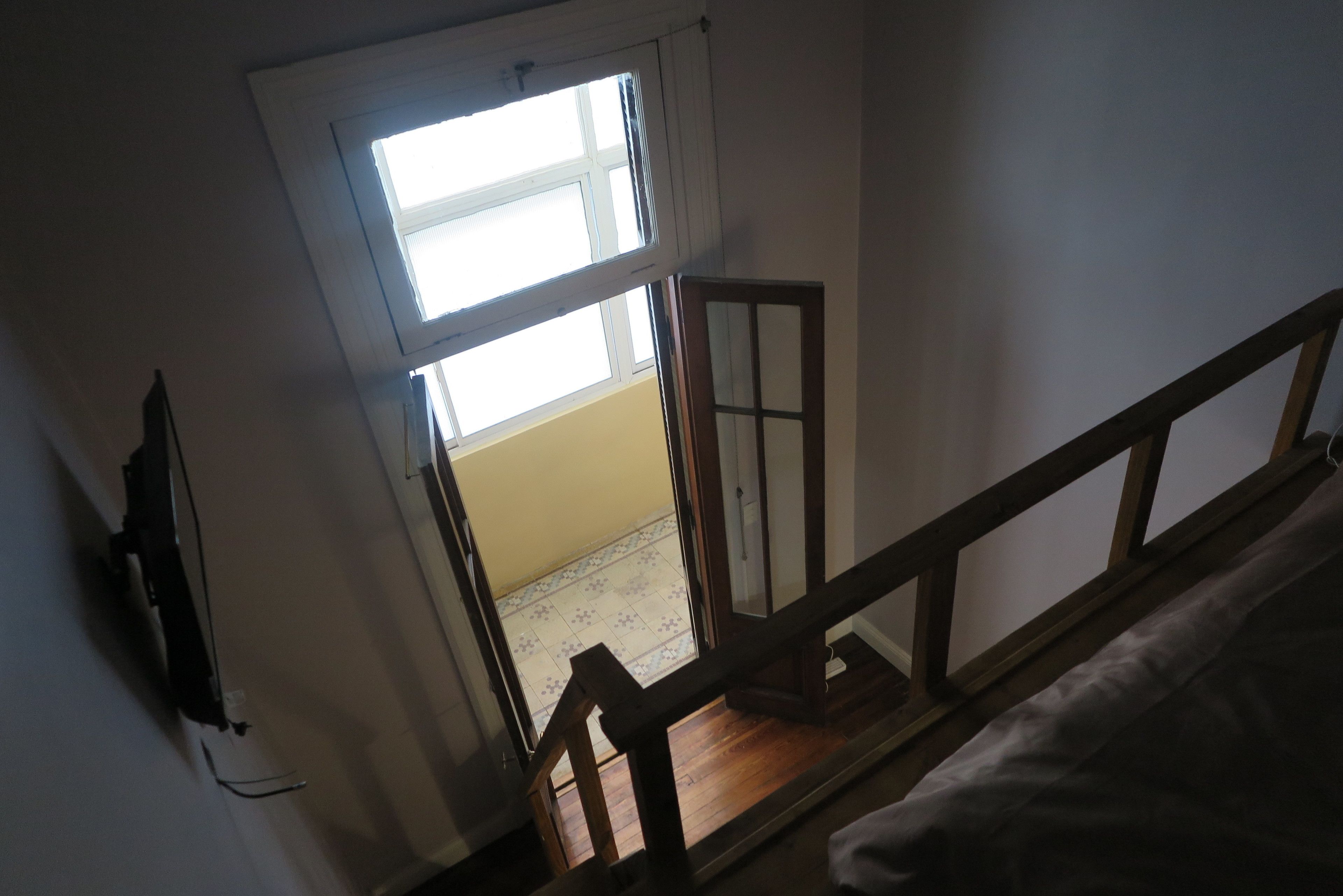 A room with a wooden staircase, a window with a view of the outside, and a door leading to another room.
