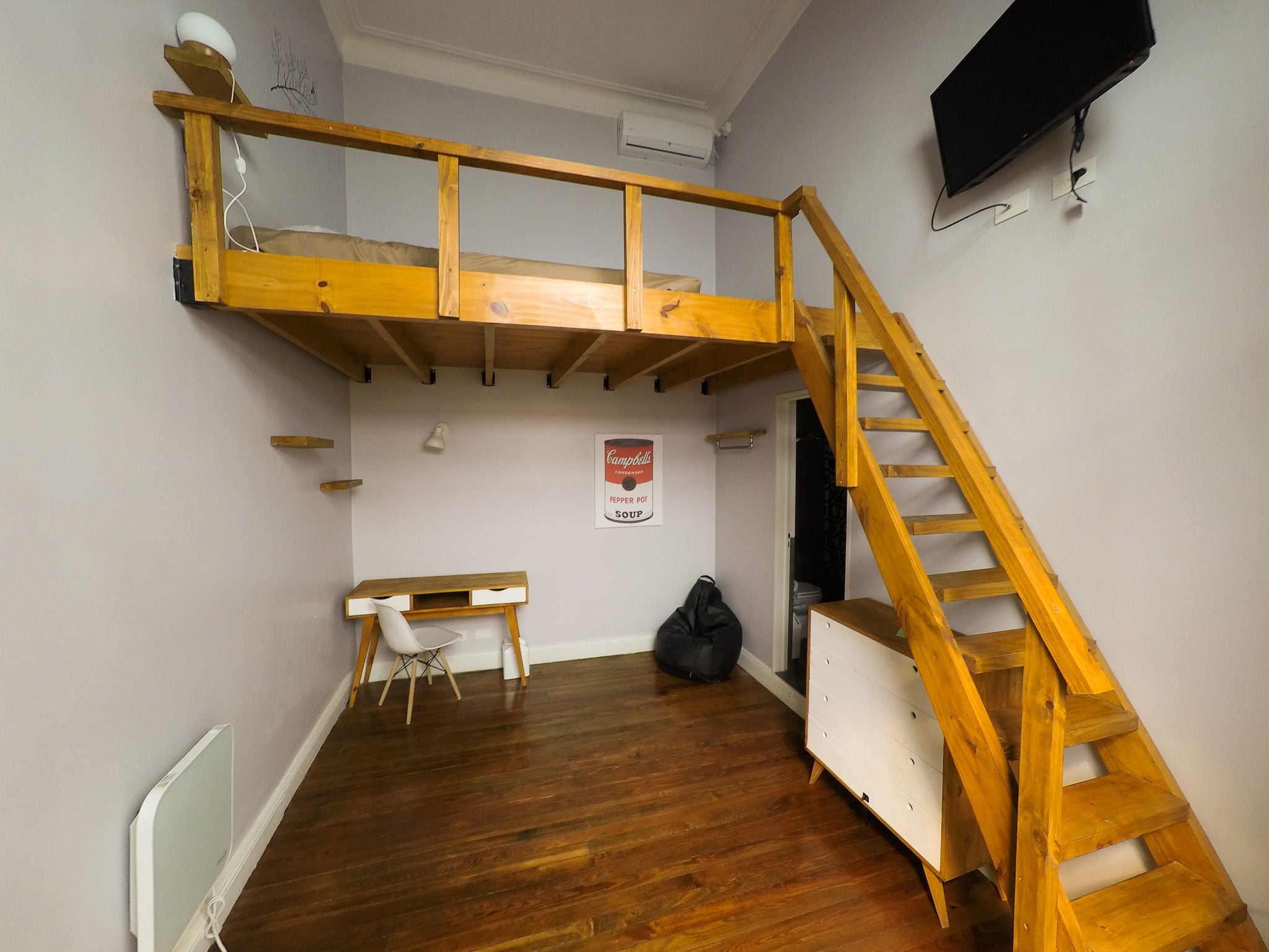 A compact room with a bunk bed, a desk, a chair, and a wooden ladder.