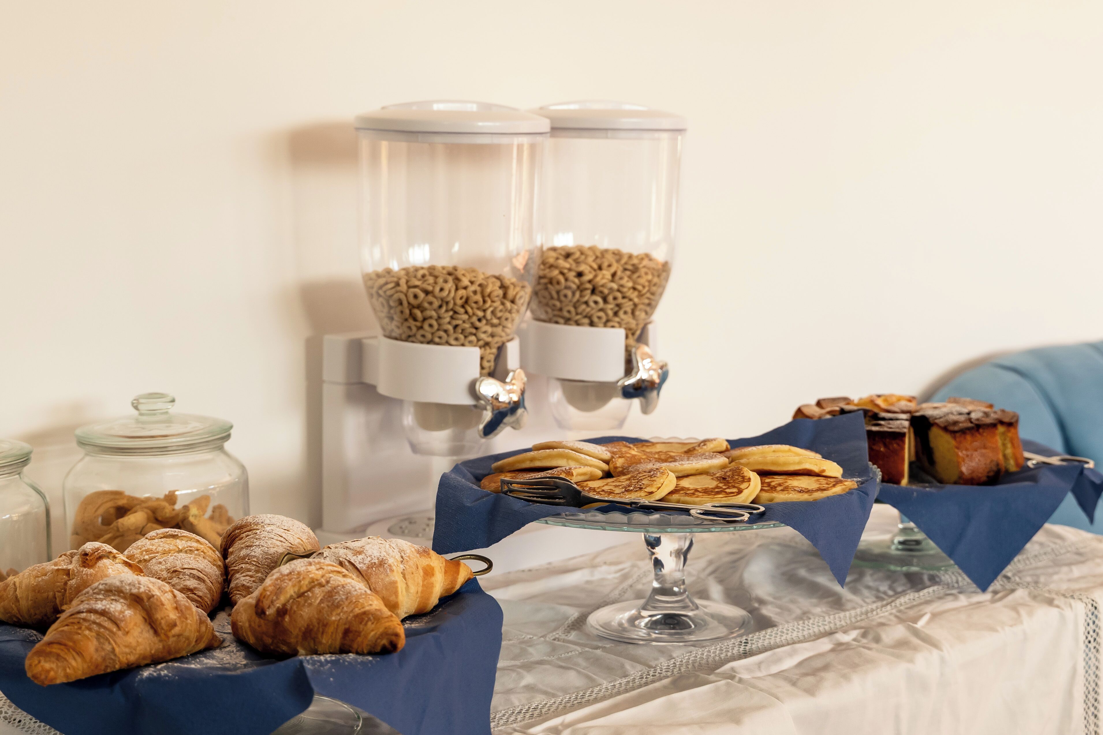 A breakfast buffet with pastries, a coffee dispenser, and a cake on a table.
