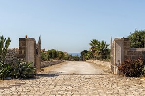 A cobblestone driveway leading to a stone gate with a view of the sea in the distance.