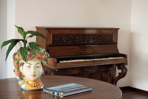 Un piano de madera con intrincados grabados, un jarrón decorativo con motivos florales y un libro sobre una mesa redonda de madera.