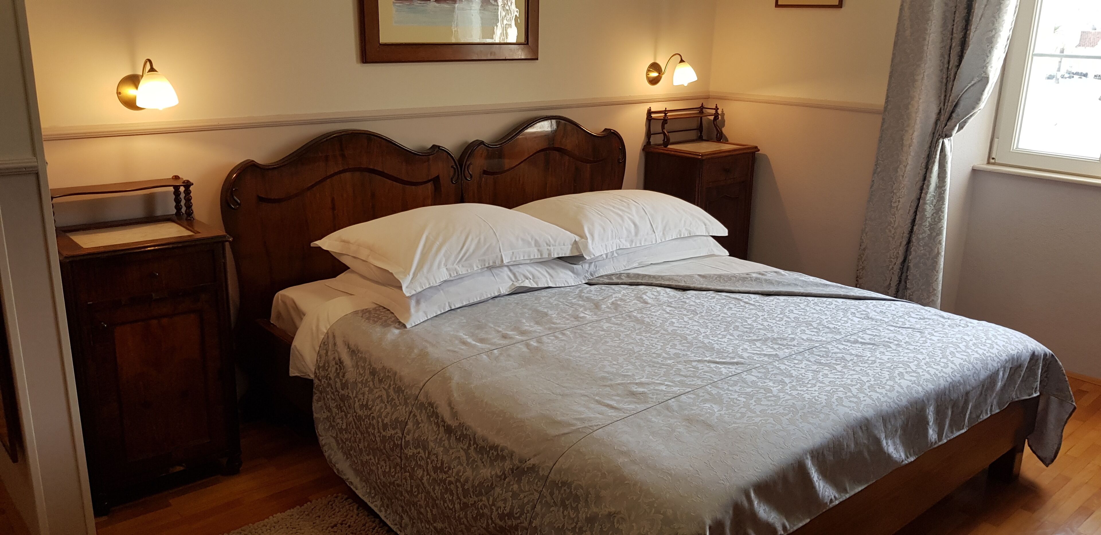 A neatly made bed with a patterned bedspread and pillows, wooden headboard, bedside tables with lamps, and a framed picture on the wall.