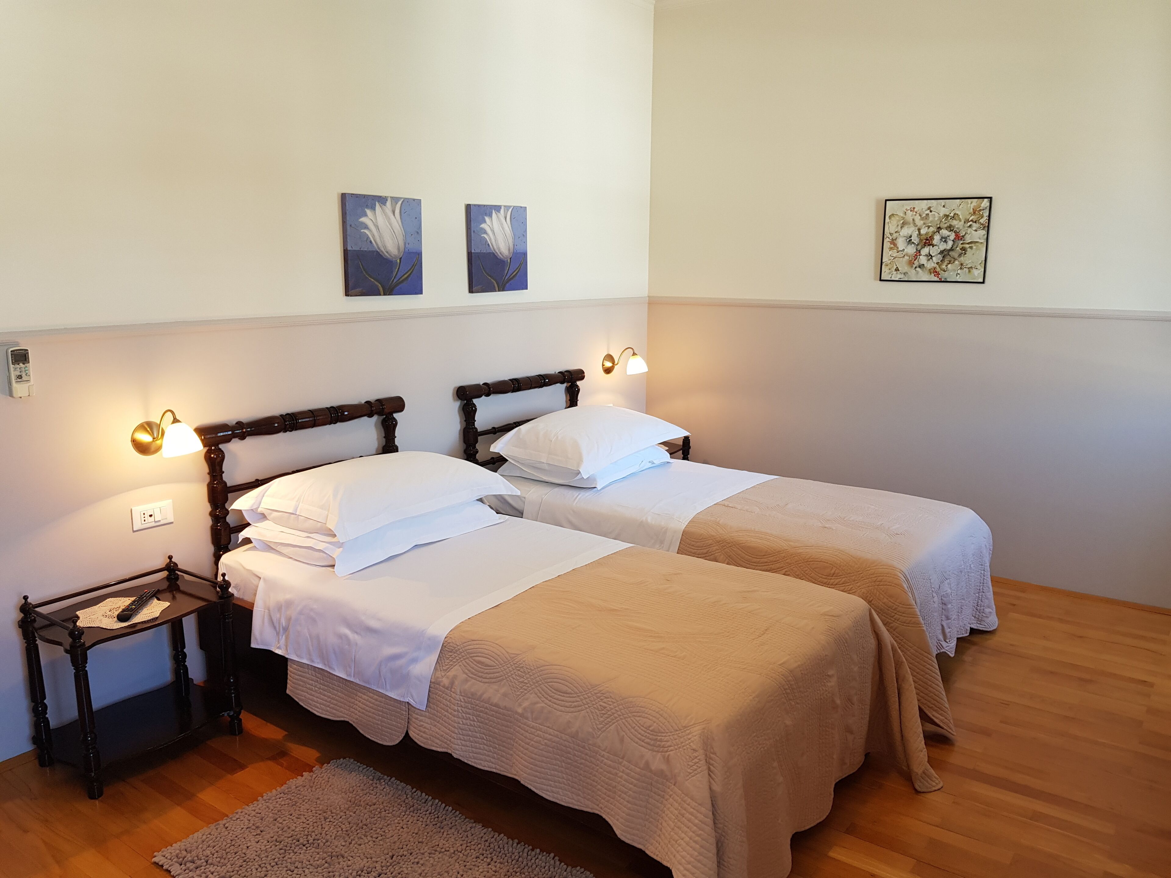 A double room with two beds, each with a wooden headboard and white bedding. There are wall-mounted light fixtures and a small table with a remote control.
