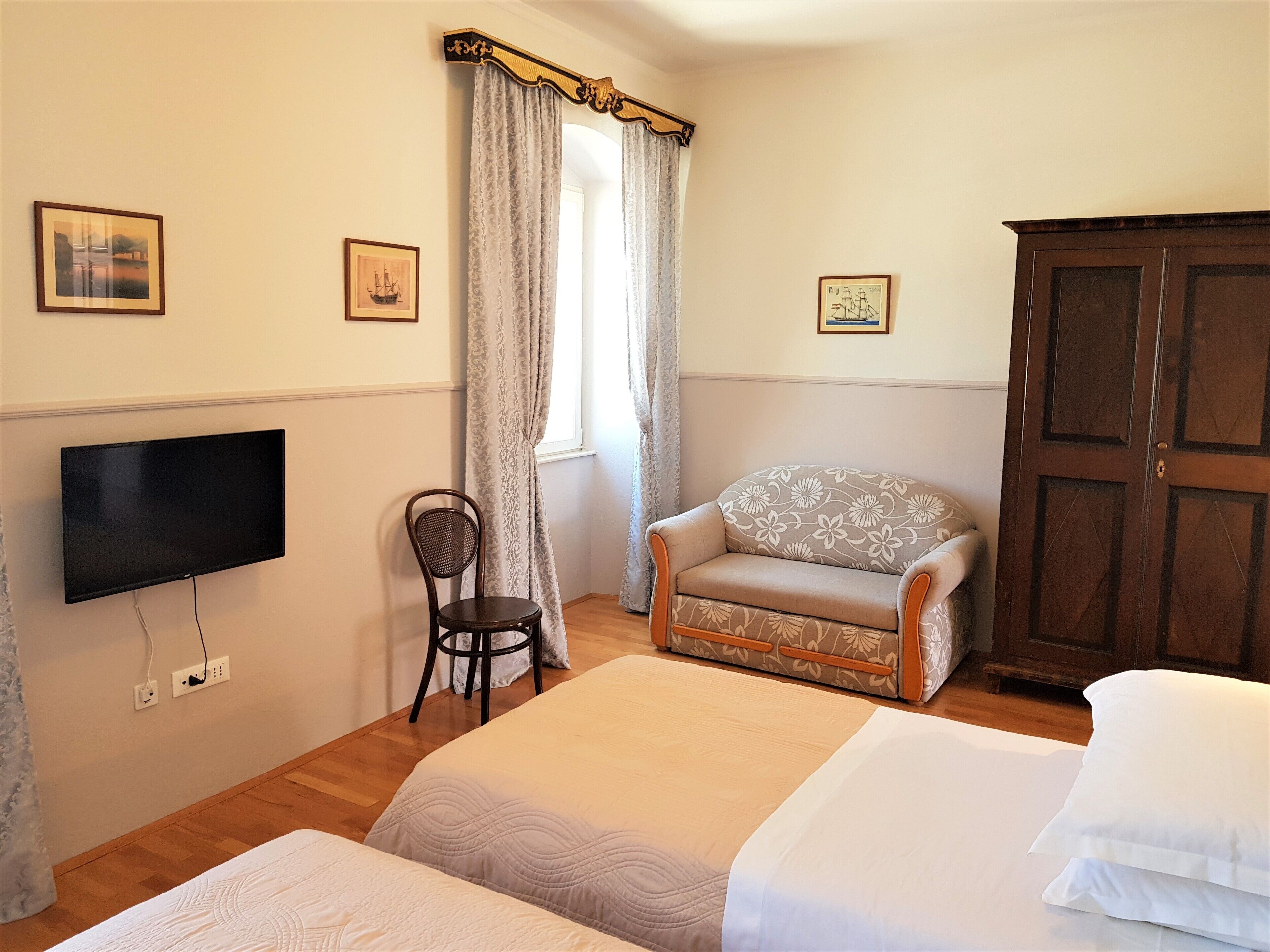 Un dormitorio con dos camas, televisión, una silla, armario y cortinas.