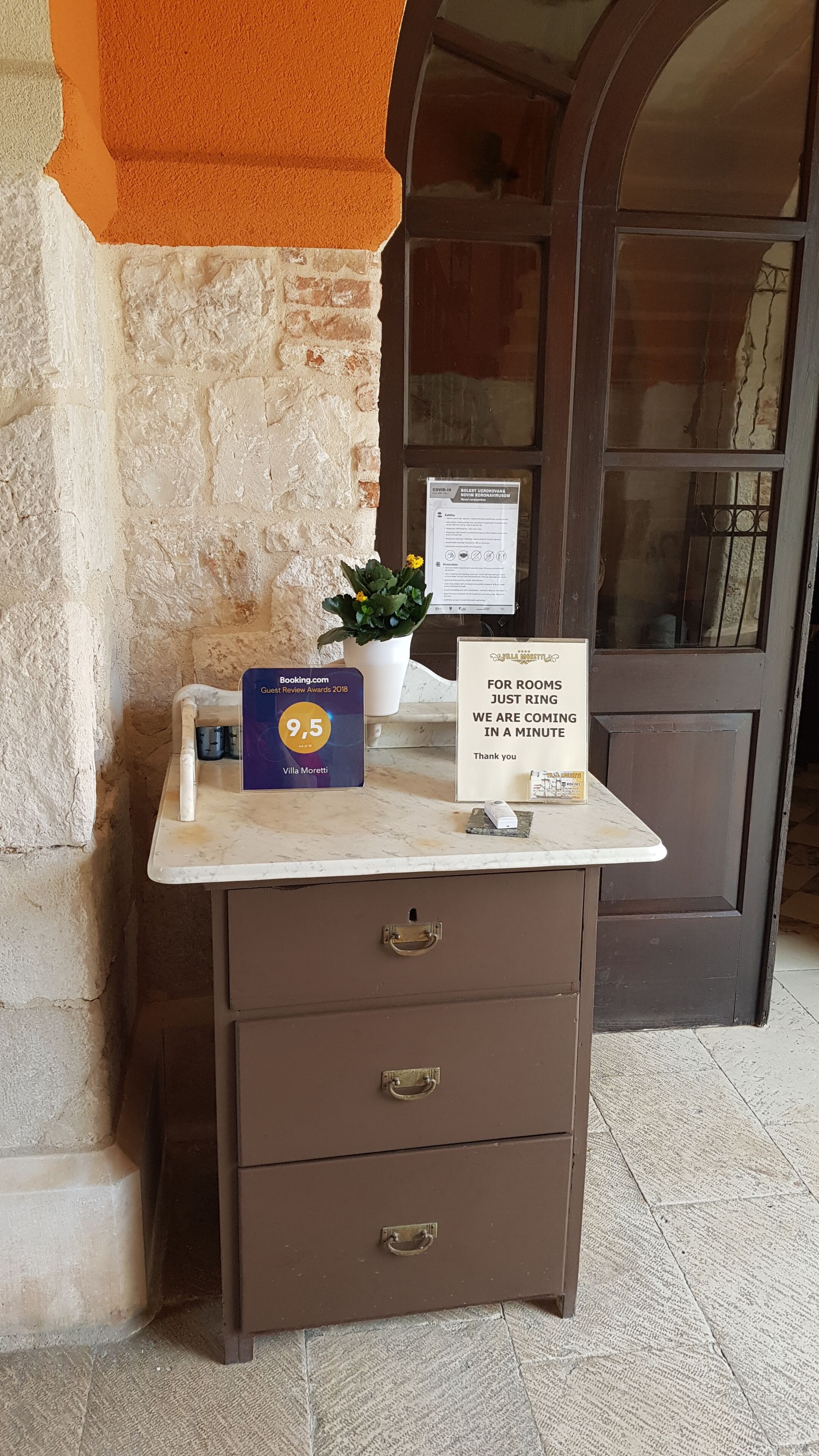 A reception desk with a plaque for the Guest Review Awards 2018, a sign for room availability, and a potted plant.