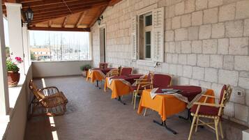 An outdoor patio with stone walls, wooden beams, and tables with orange tablecloths and wooden chairs.