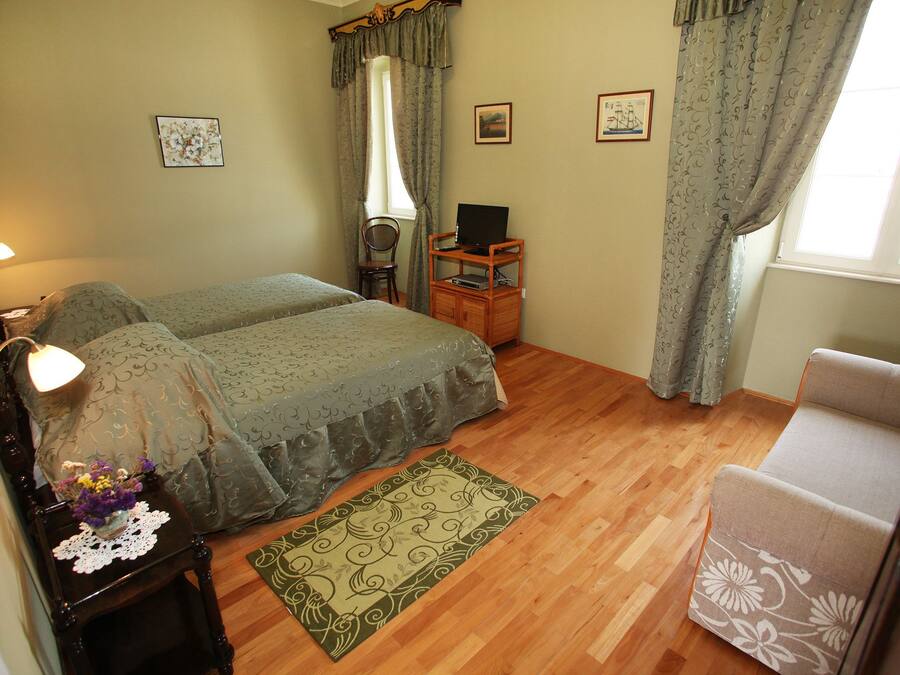 A bedroom with two beds, a wooden nightstand, a TV stand, a chair, and a window with curtains.
