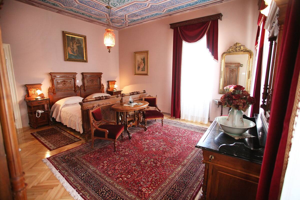Quarto tradicional com cama, mesa, cadeira, espelho e um vaso de flores.