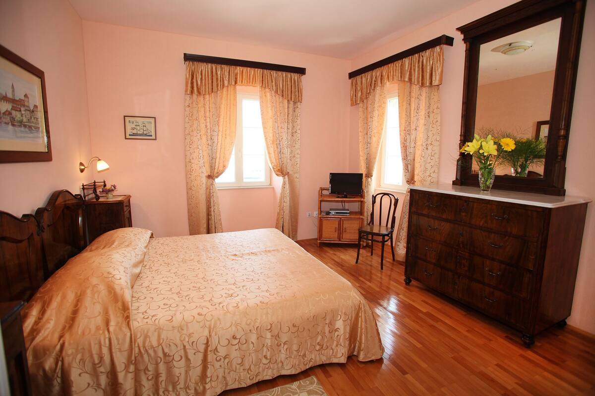 Quarto com cama, escrivaninha com computador, cadeira, cômoda e espelho.