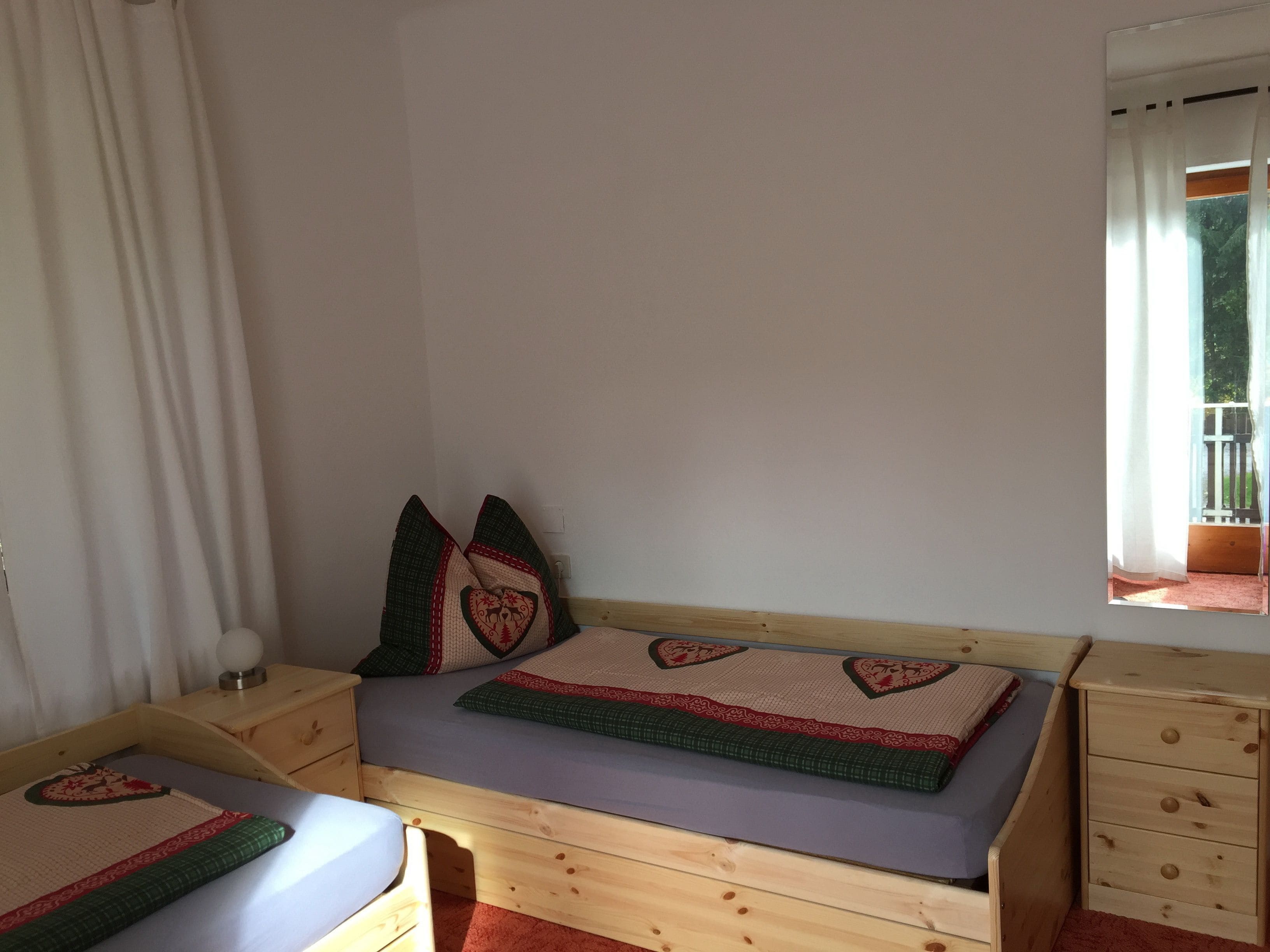 Una habitación pequeña y acogedora con una cama individual, una mesita de noche y una ventana con cortinas.