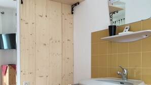 A bathroom with a wooden door, a white sink with a mirror above it, and a yellow-tiled wall. - Pension Waldkrieber (Hermagor-Pressegger See)