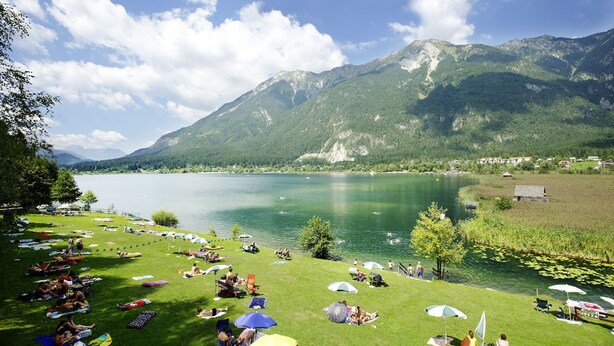 A lakeside view with a grassy area, tents, and a mountain backdrop. - Pension Waldkrieber (Hermagor-Pressegger See)
