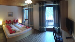 A bedroom with a bed, a bedside table, a lamp, a window with curtains, a chair, and a television. - Pension Waldkrieber (Hermagor-Pressegger See)