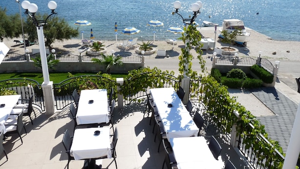 Un restaurant en bord de mer, doté d’une terrasse offrant une vue sur un lac paisible, des bateaux au loin et un paysage vallonné en arrière-plan.