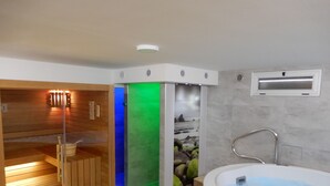 Un sauna avec des bancs en bois et un espace séparé avec un bain à remous, le tout agrémenté d’un mur en pierre en arrière-plan.