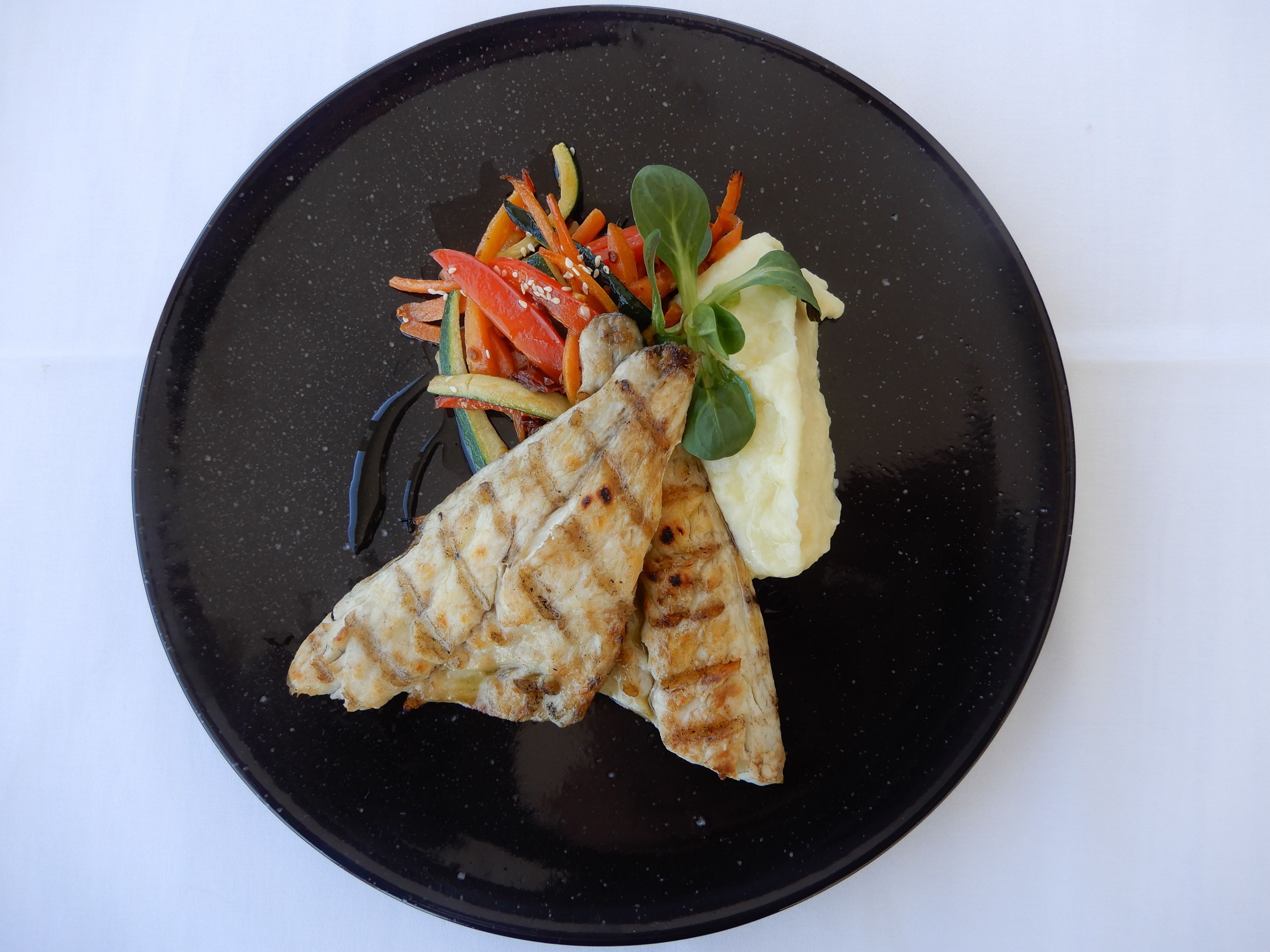 Une assiette noire contenant du poulet grillé, une salade en accompagnement et de la purée de pommes de terre.