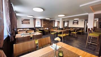 A restaurant with multiple tables and chairs, wooden flooring, and a stone wall.