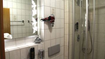 A bathroom with a mirror, a hairdryer mounted on the wall, a soap dispenser, and a shower area.