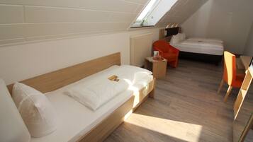 Habitación de hotel compacta con tragaluz, una cama individual, una mesita pequeña con una silla, y un área de descanso separada con otra silla.