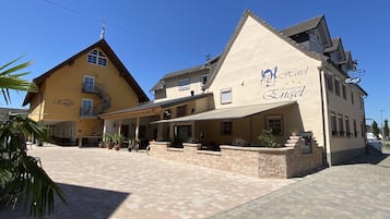 Hotel Engel offers a traditional facade with a pitched roof and balcony, welcoming guests through a covered walkway with potted plants and outdoor seating.